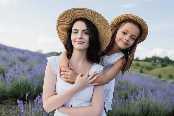 Happy girl in straw hat hugging mother in blurred field — Stockfoto