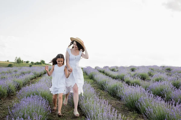 Весела мати і дочка в білих сукнях тримаються за руки під час бігу на лузі — стокове фото