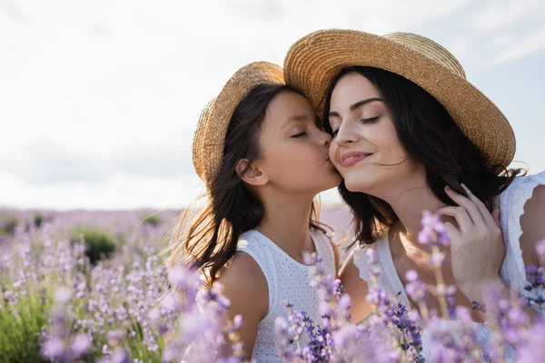 Child kissing woman smiling with closed eyes in flowering field — Stockfoto