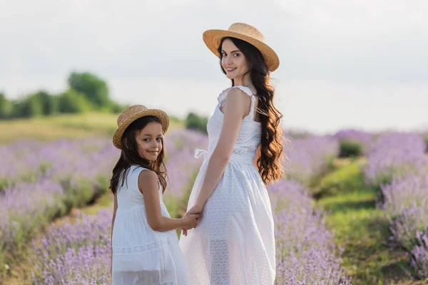 Joyful girl and woman with long hair looking at camera and holding hands in meadow — Stock Photo