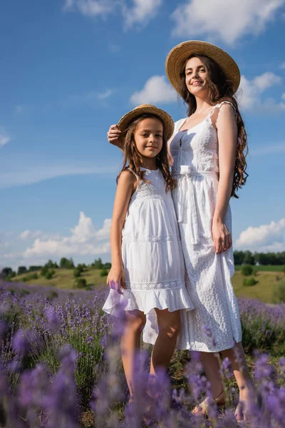 Низкий угол зрения мамы и дочери в белых платьях, стоящих в цветущем поле — стоковое фото