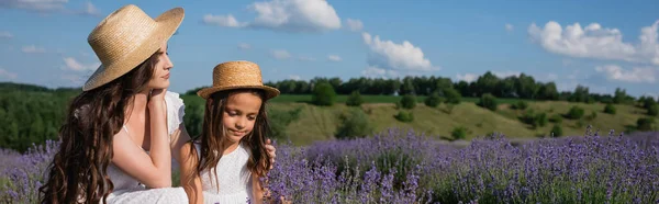 Brunette woman in straw hat hugging daughter in lavender meadow, banner — Stock Photo