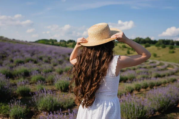 Back view of child with long hair holding straw hat while standing in meadow — Fotografia de Stock