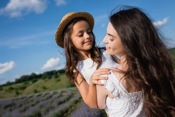 Brunette woman with long hair holding daughter in straw hat outdoors — Foto stock