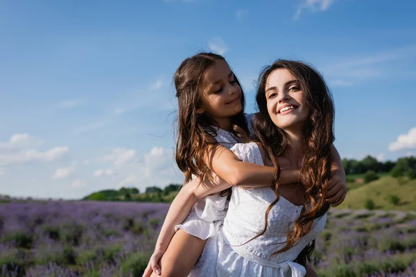 Excited woman piggybacking daughter in blurred lavender field — Fotografia de Stock