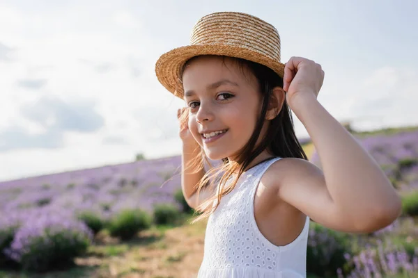 Pleased girl in straw hat looking at camera in blurred lavender meadow — Photo de stock