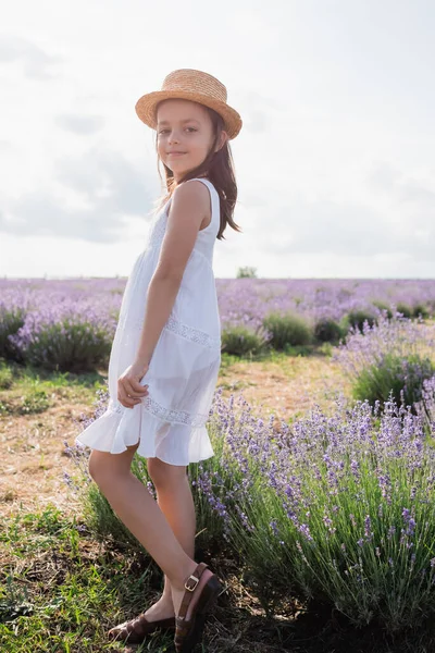 Child in white dress and straw hat smiling at camera in lavender meadow — Foto stock