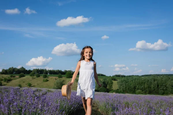 Happy girl in summer dress walking in lavender field under blue sky with white clouds — Photo de stock
