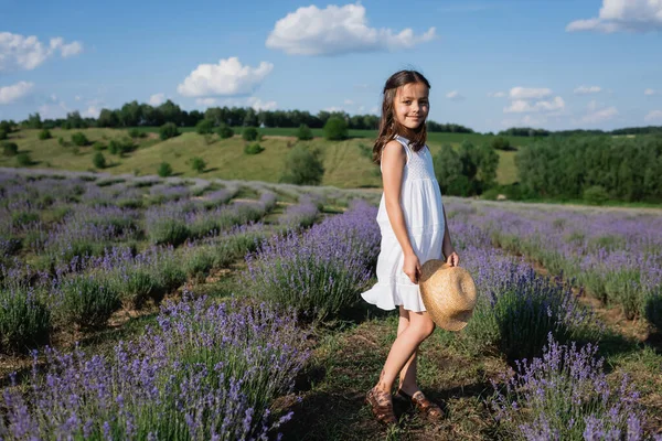 Full length of smiling girl with straw hat standing in lavender field and looking at camera — Photo de stock