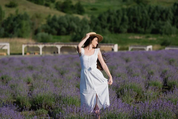 Woman in white dress and straw hat posing in field with blossoming lavender — Photo de stock