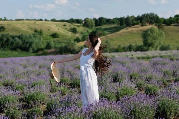 Woman with long hair and straw hat standing in lavender field in white dress - foto de stock