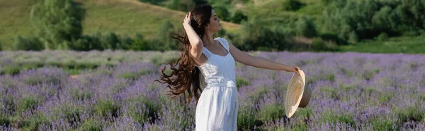 Woman in white dress touching long hair and holding straw hat in lavender field, banner — Stock Photo