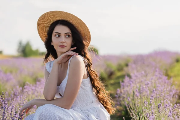 Pretty woman with long hair and in straw hat looking away in meadow - foto de stock