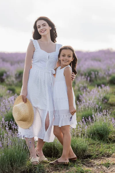 Happy mother and daughter in white summer dresses smiling at camera in field — Fotografia de Stock