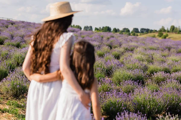 Back view of blurred mother and daughter in straw hats hugging in lavender field — Foto stock