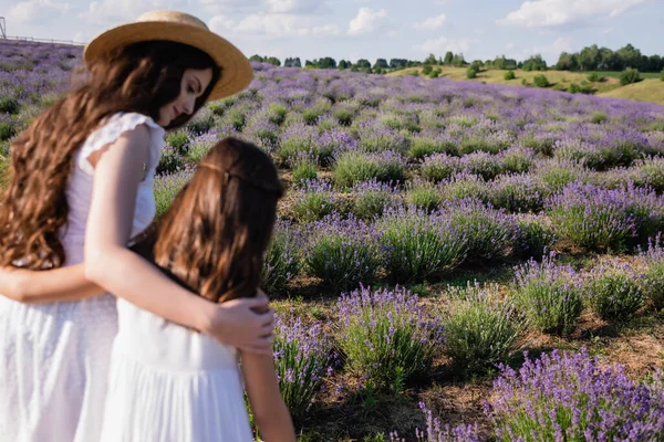 Brunette woman hugging daughter in lavender field on blurred foreground — Stock Photo