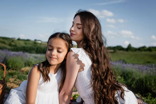 Woman and child with long hair and closed eyes sitting in blurred meadow — Foto stock