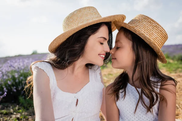 Cheerful mother and daughter in straw hats smiling with closed eyes outdoors — Fotografia de Stock