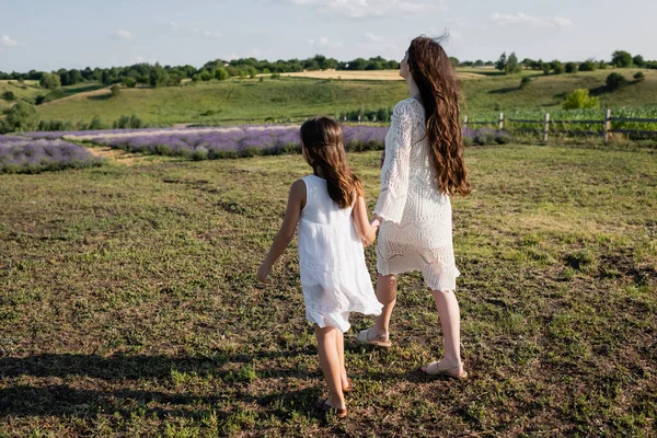 В полный рост мать и дочь в белых платьях идут по полю — стоковое фото