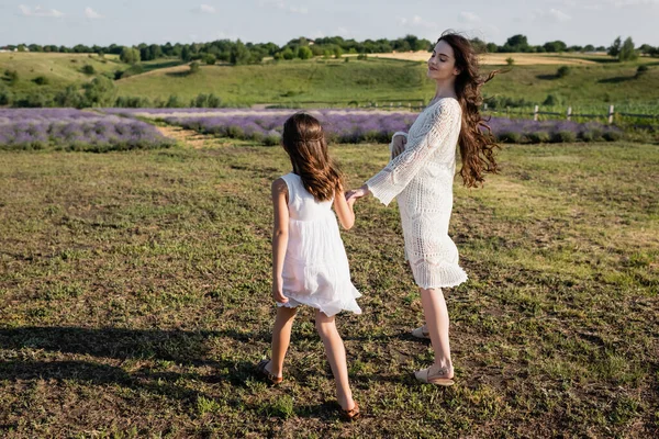 Happy pregnant woman holding hands with daughter while walking in field — Stock Photo