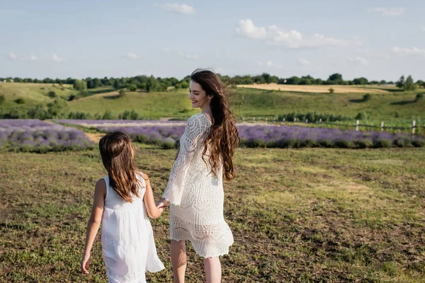 Smiling pregnant woman in openwork dress walking with daughter in countryside — Photo de stock