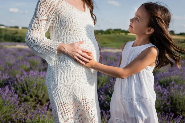 Side view of brunette girl touching belly of pregnant mom outdoors — Stock Photo