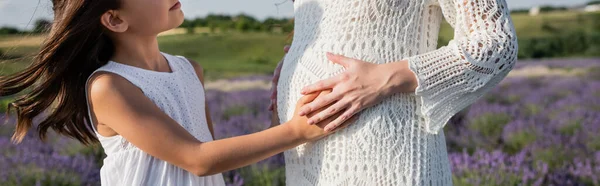 Partial view of child touching tummy of pregnant mother in blurred field, banner — Stockfoto