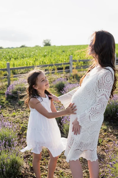 Smiling girl touching tummy of pregnant mom in field — Foto stock