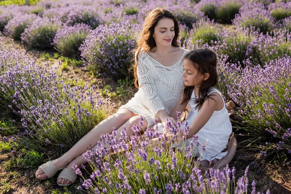 Brunette pregnant woman sitting with daughter in flowering field — Fotografia de Stock