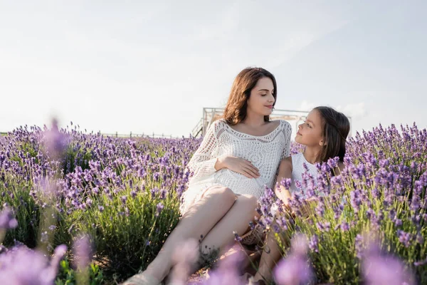 Веселая девушка и беременная женщина смотрят друг на друга в лавандовом поле — стоковое фото