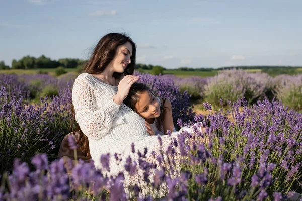 Happy pregnant woman with daughter embracing in blurred lavender meadow — Foto stock