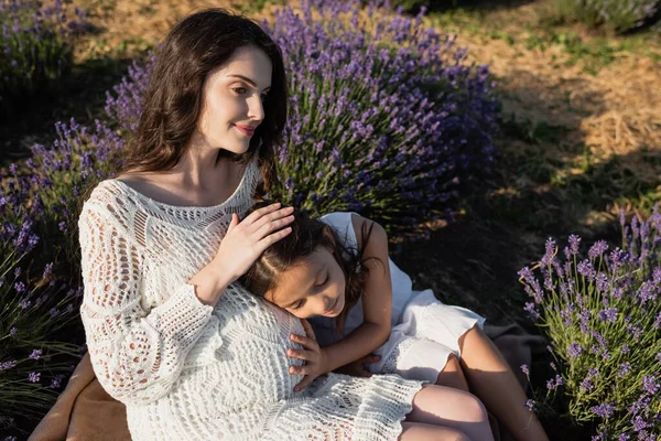 High angle view of smiling pregnant woman with child sitting in blooming field - foto de stock