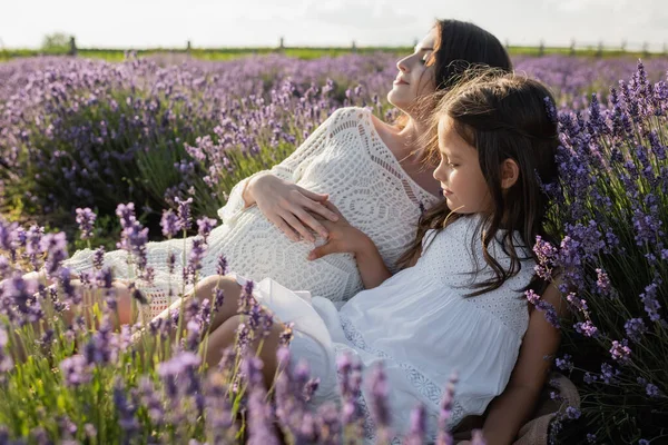 Pregnant woman and girl in white dresses in meadow with blooming lavender — Foto stock