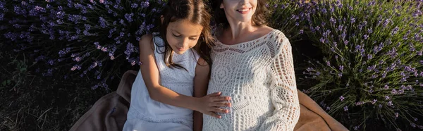 High angle view of happy pregnant woman in openwork dress near daughter in lavender field, banner — Photo de stock