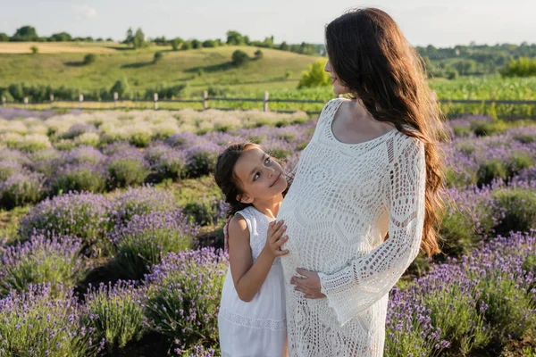 Cheerful child embracing pregnant mom in field with blossoming lavender — Foto stock