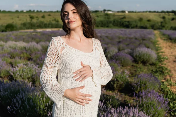 Pregnant brunette woman in white dress in blurred field with blossoming lavender — Stock Photo