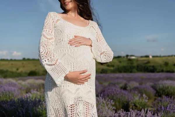Обрезанный вид беременной женщины в платье, обнимающей животик на открытом воздухе — стоковое фото