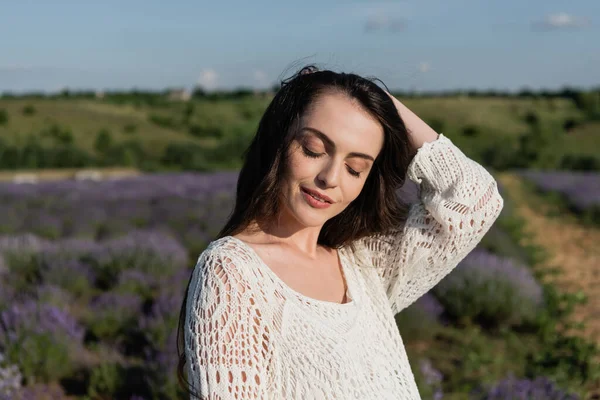 Pretty woman with closed eyes adjusting long hair in blurred field — Stockfoto