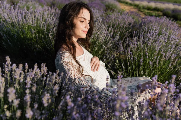 Pregnant woman with long hair enjoying sitting in lavender field — Stockfoto