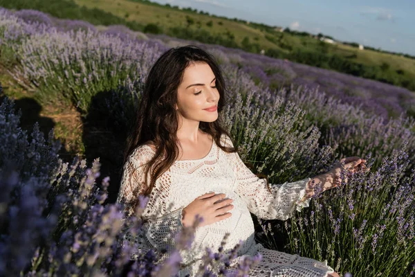 Pleased pregnant woman in openwork dress sitting in lavender field — Stock Photo