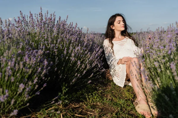 Беременная женщина с закрытыми глазами сидит в поле с цветущей лавандой — стоковое фото