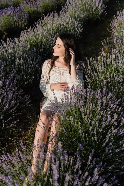 Высокий угол обзора беременной женщины, сидящей рядом с цветущей лавандой в поле — стоковое фото