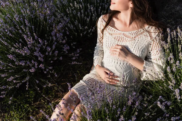 Partial view of happy pregnant woman in openwork dress sitting in lavender meadow — Stock Photo