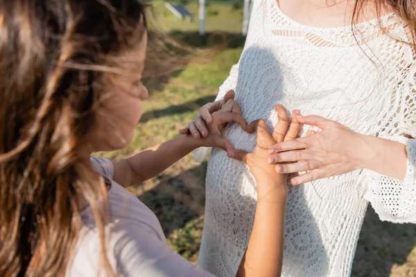 Розмита дівчина показує знак серця біля живота вагітної матері — стокове фото