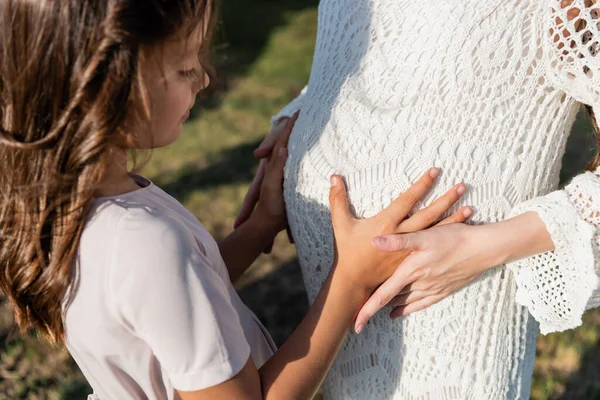 Blurred child touching belly of mother in white openwork dress — Stock Photo