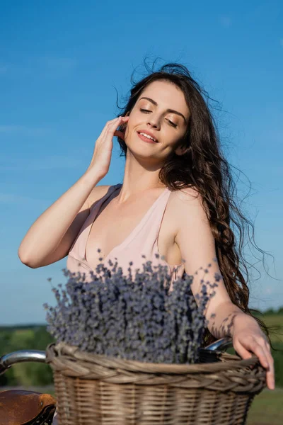 Pretty brunette woman with long hair smiling near blurred lavender flowers - foto de stock