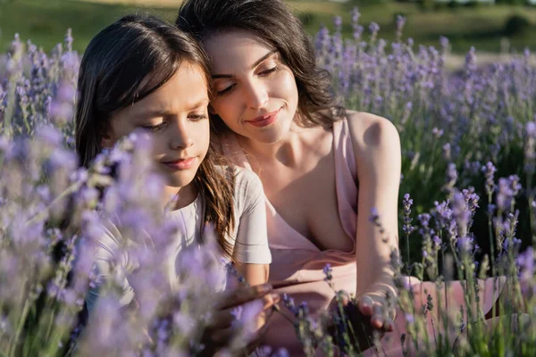 Happy woman and child with brunette hair near blurred lavender in field - foto de stock