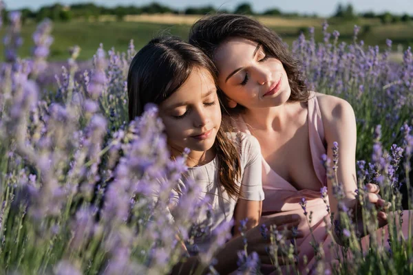 Довольные мама и дочь с закрытыми глазами на лугу с цветущей лавандой — стоковое фото