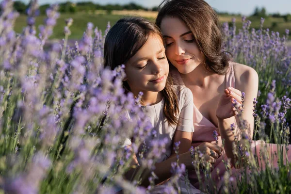 Happy mom and daughter with long hair and closed eyes in blurred lavender field — Stockfoto