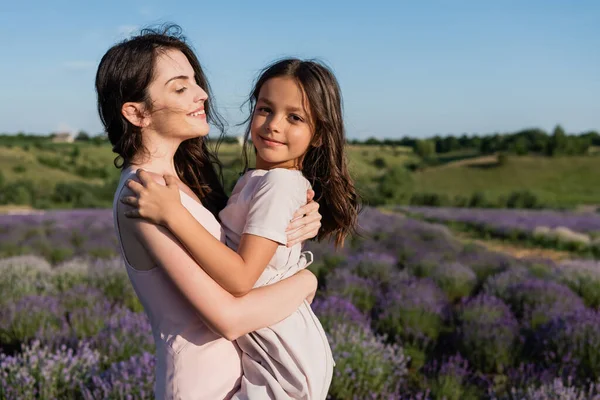 Brunette woman embracing daughter smiling at camera in lavender meadow — Stockfoto